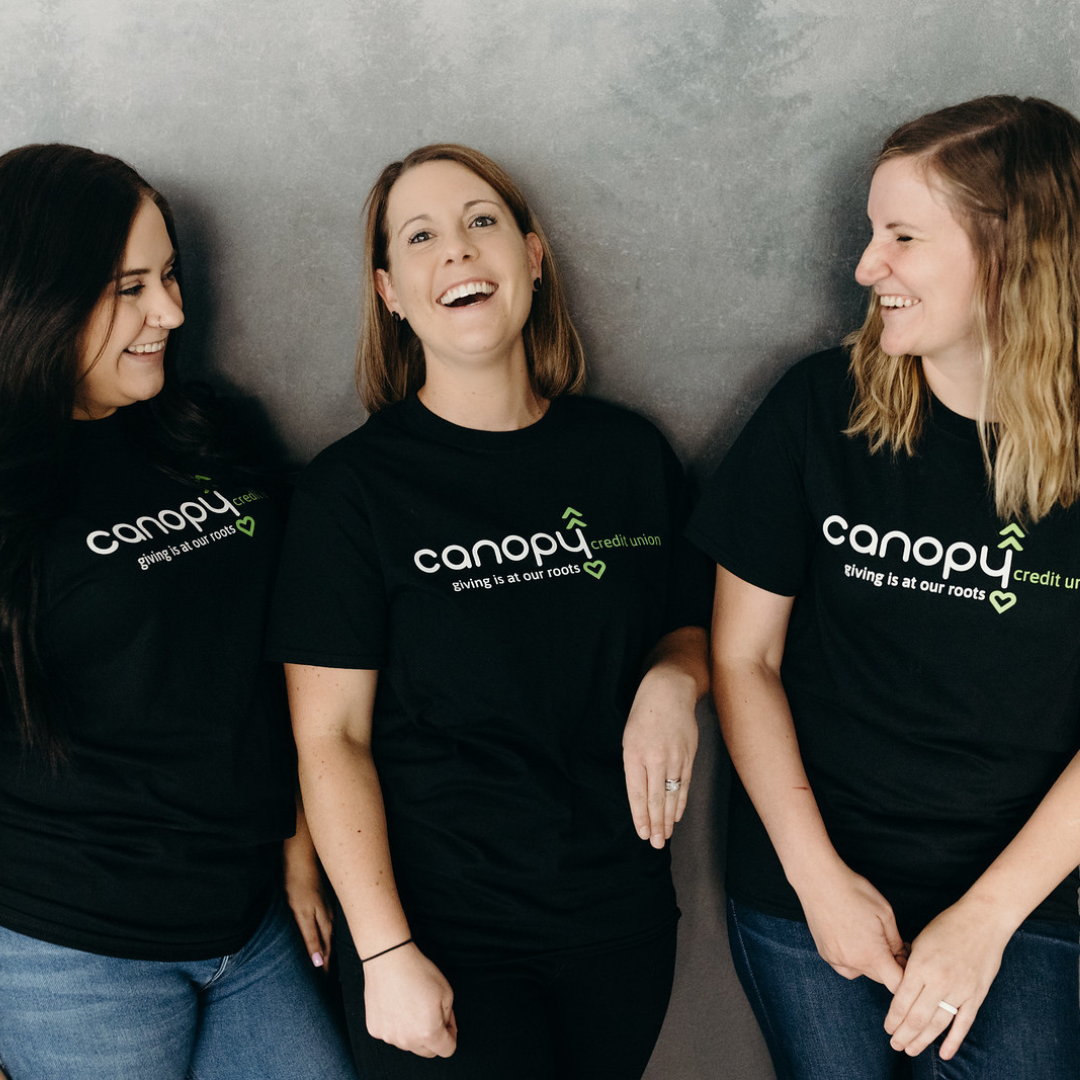 Three women stand, smiling.