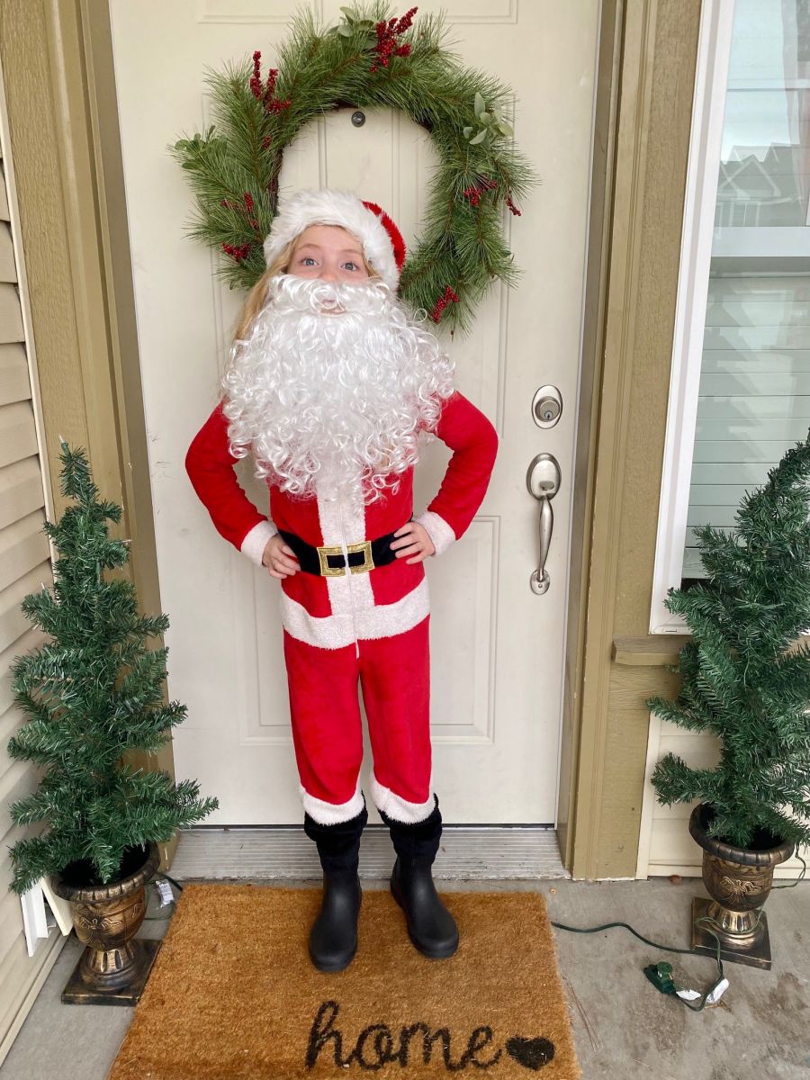 picture of young girl dressed as Santa clause standing in front of Christmas wreath